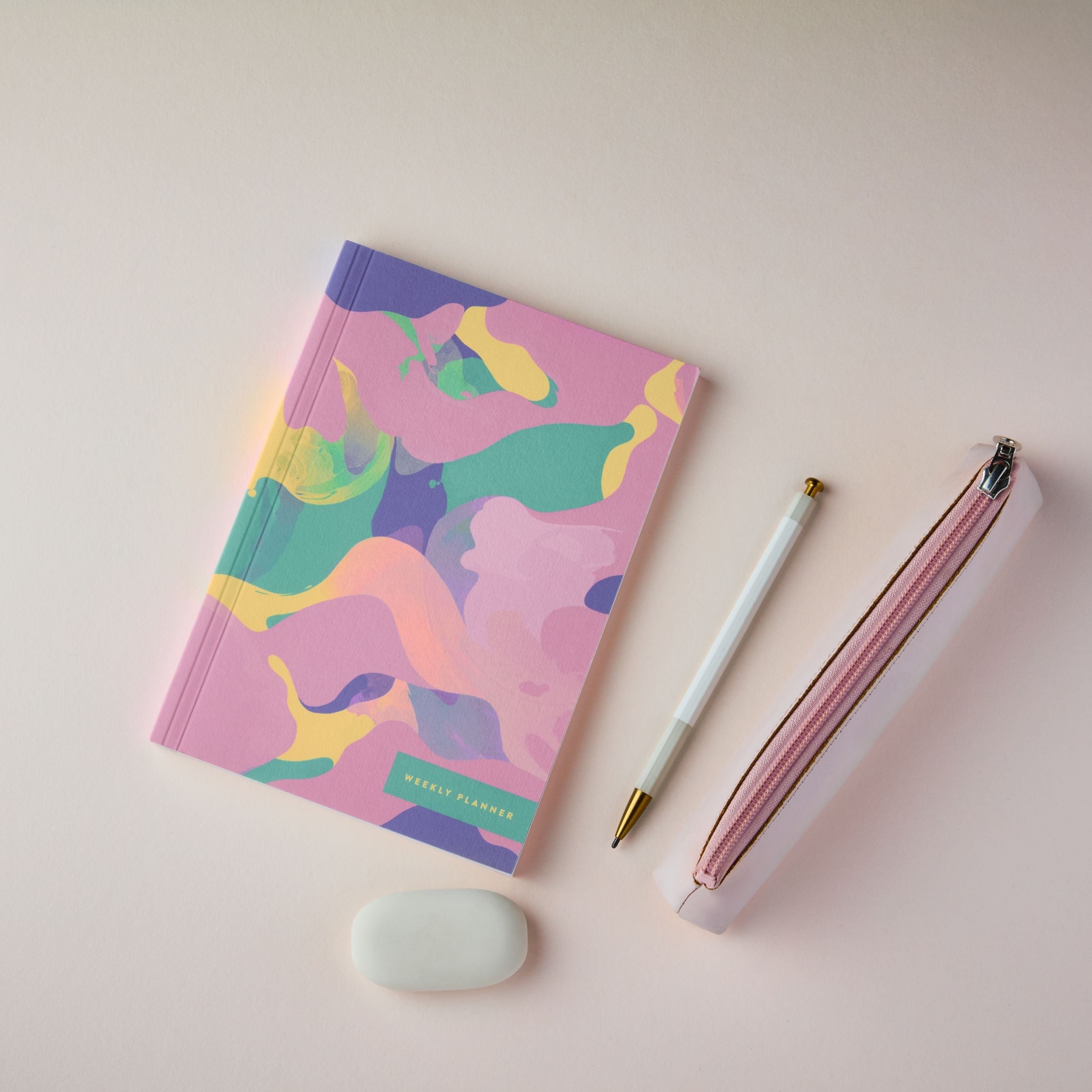 The Reverie A5 Weekly Planner Pink Marble with a pen and eraser on a light pink background