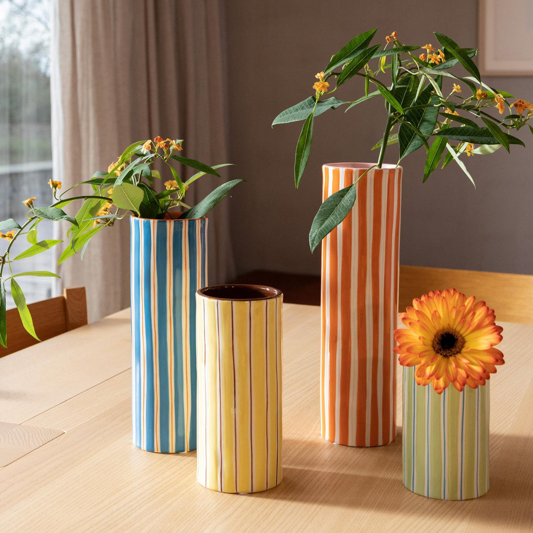 Pink and orange striped vase alongside other striped vases, all displayed on a wooden table with colorful flowers arranged inside them.