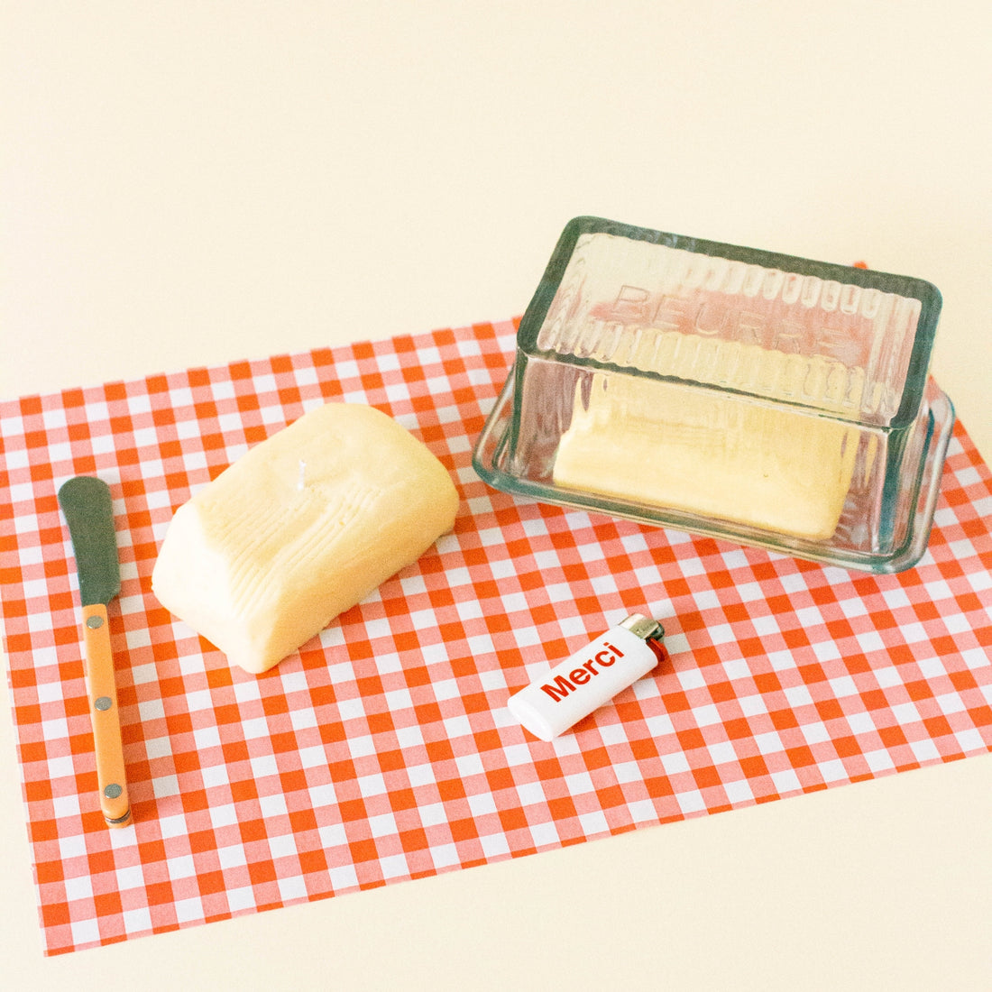 Butter candle, knife, and glass container on a red and white checkered tablecloth