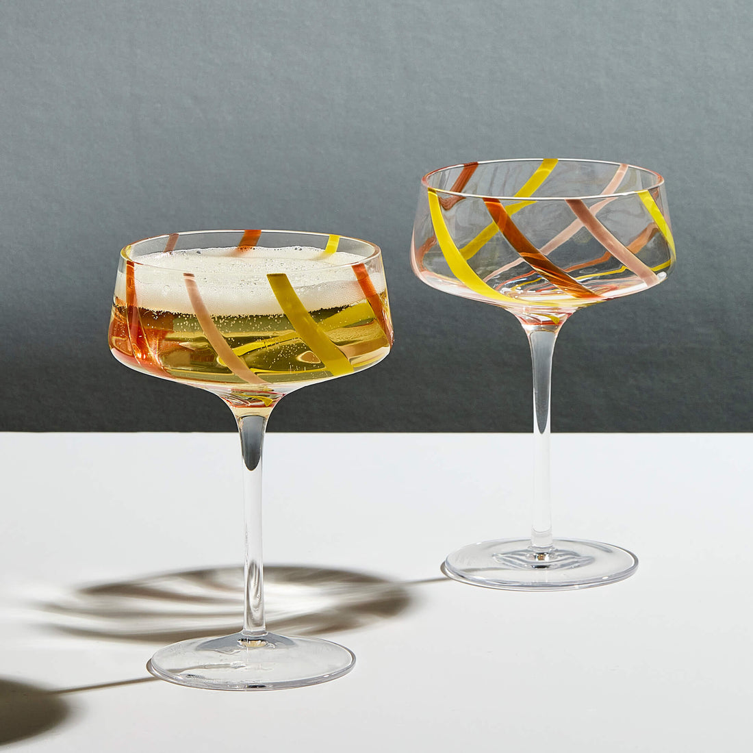 Two citrus swirl champagne glasses filled with champagne on a grey background
