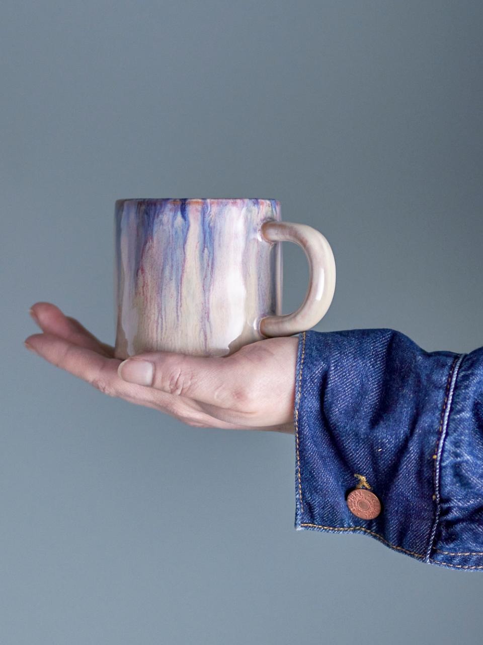Hand holding the Amalia Blue Ceramic mug with a blue and beige design against a gray background