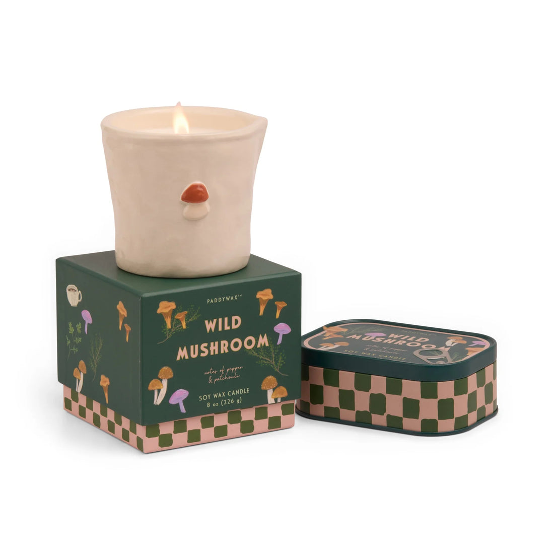 Candle with mushroom design on top, next to its packaging and mushroom tin candle against a white background