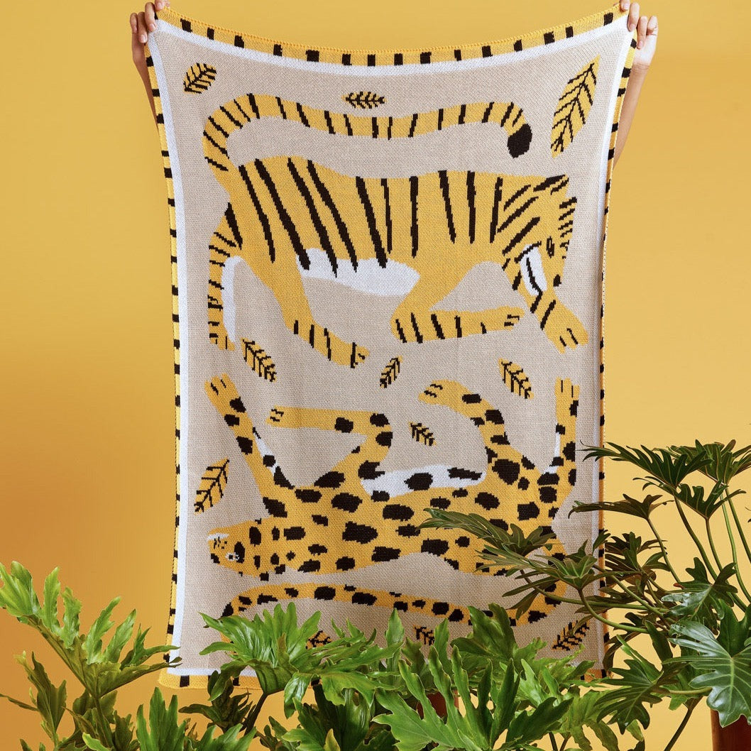 A person holding the Big Cats Mini Blanket 30x40 inches, designed by James Daw, featuring two big cats and leaves, made from 50% cotton and 50% recycled polyester, soft and eco-friendly, made in USA
