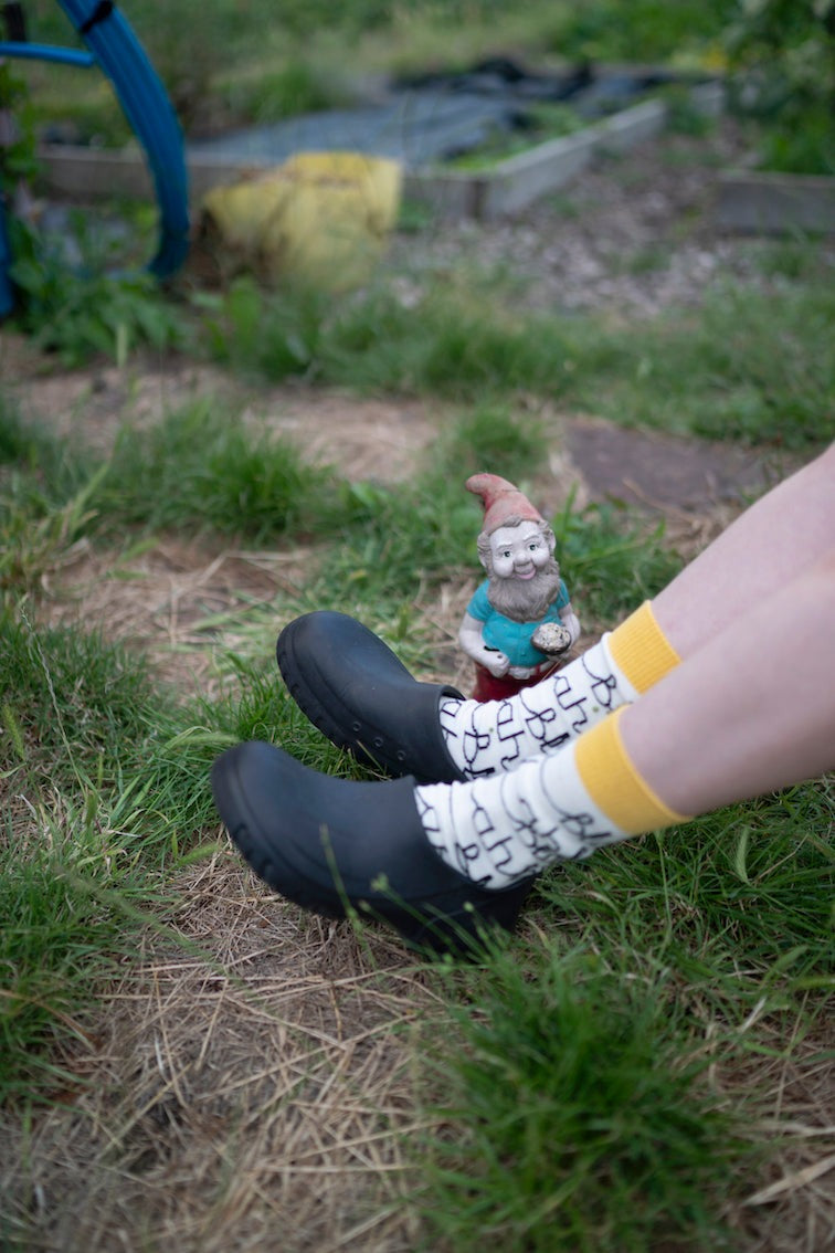 Person wearing black shoes and the blah blah socks with a garden gnome on grass