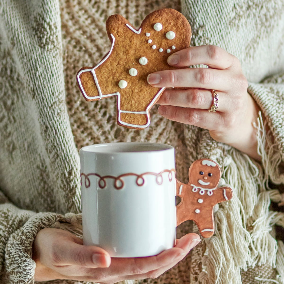 Person holding the Hand-painted Ginnie Mug in brown stoneware with a festive gingerbread-shaped handle, perfect for hot chocolate, coffee, or tea during Christmas.