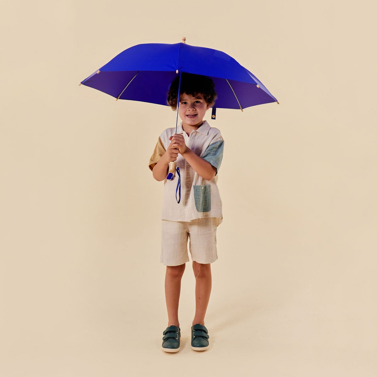 Child holding a blue umbrella against a beige background