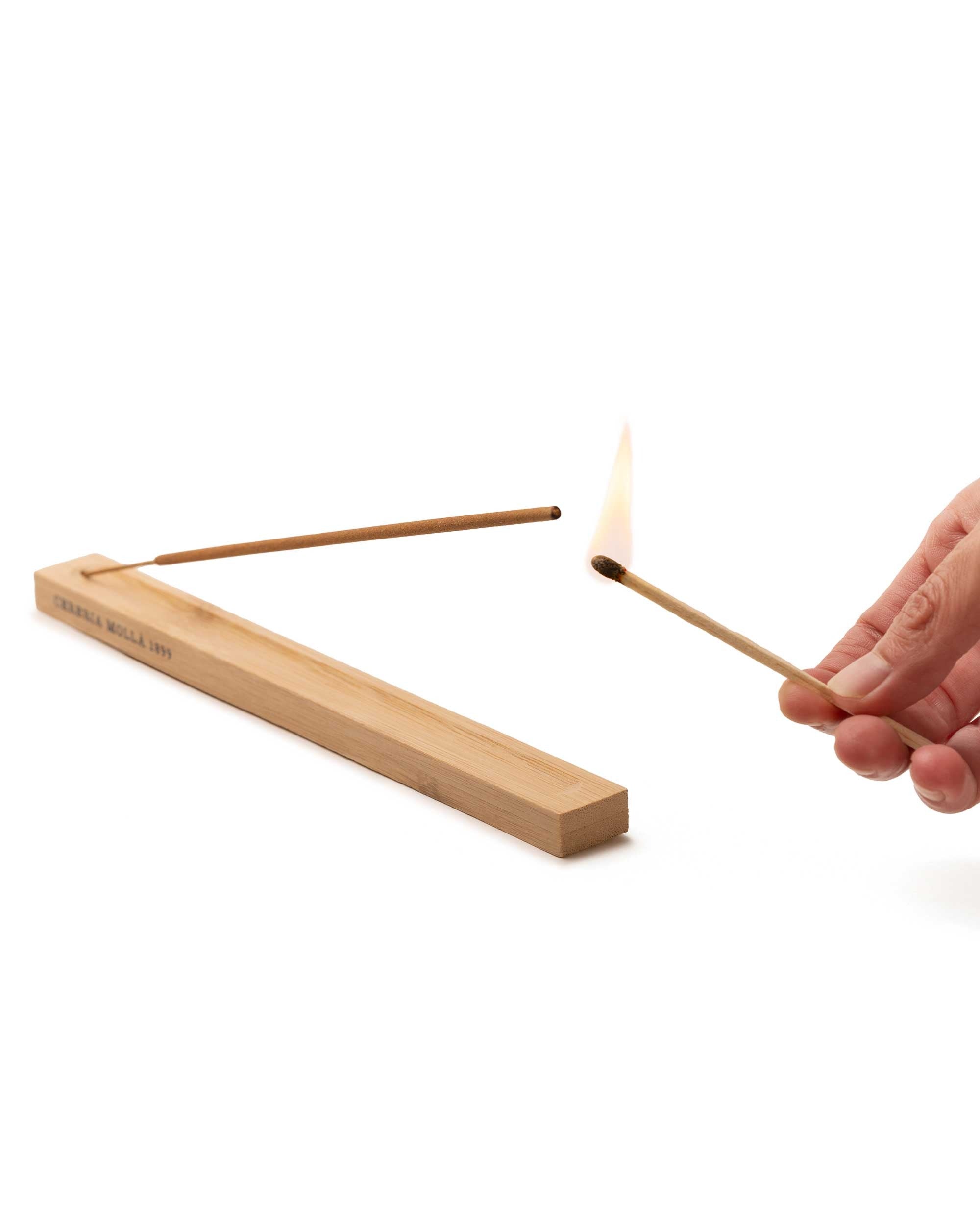 Person lighting the Bulgarina Rose & Oud wooden incense stick with a match on a white background