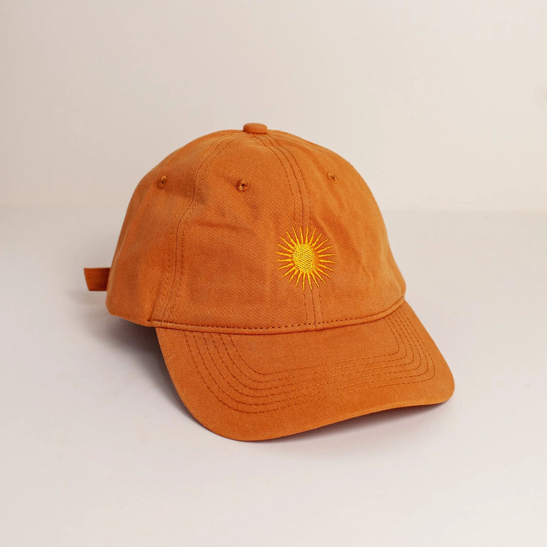 Orange cotton cap with gold embroidered sun design on the front, displayed against a grey background