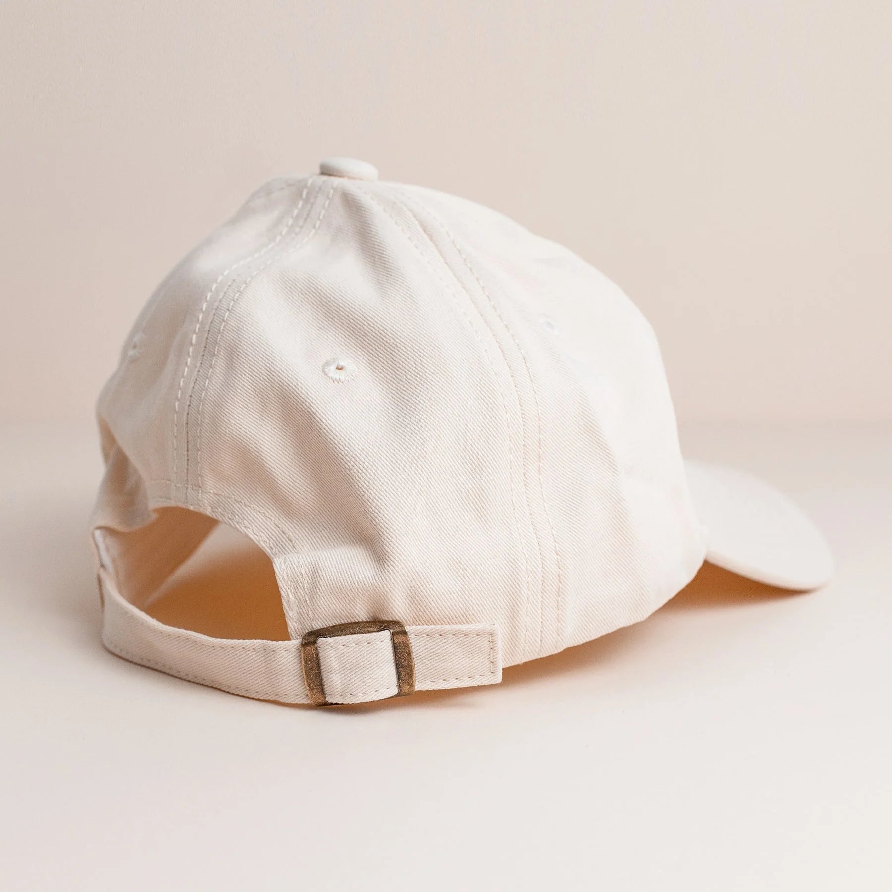 Off White cap with copper embroidered design palm on the front, featuring an adjustable brass closure and a back popper button for ponytail access.