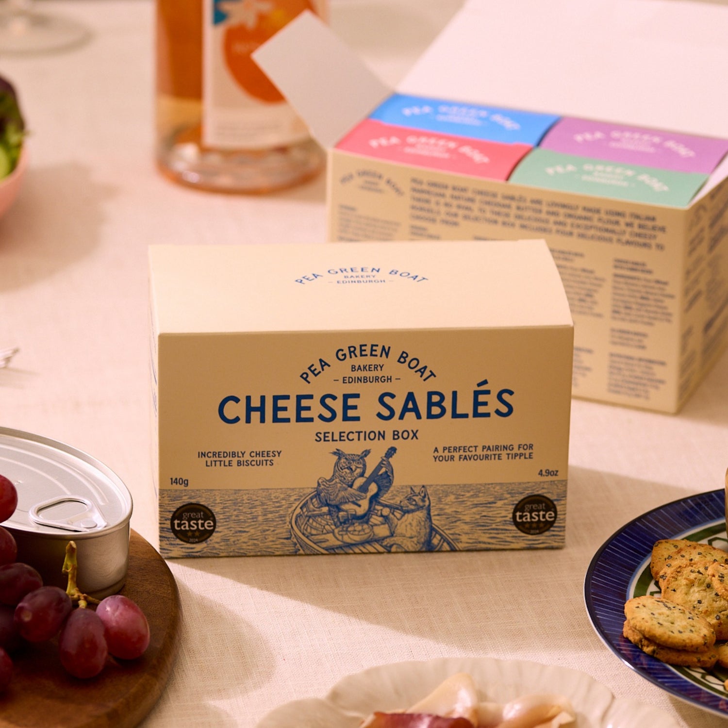 Box of Cheese Sablés selection on a table with grapes and cookies.