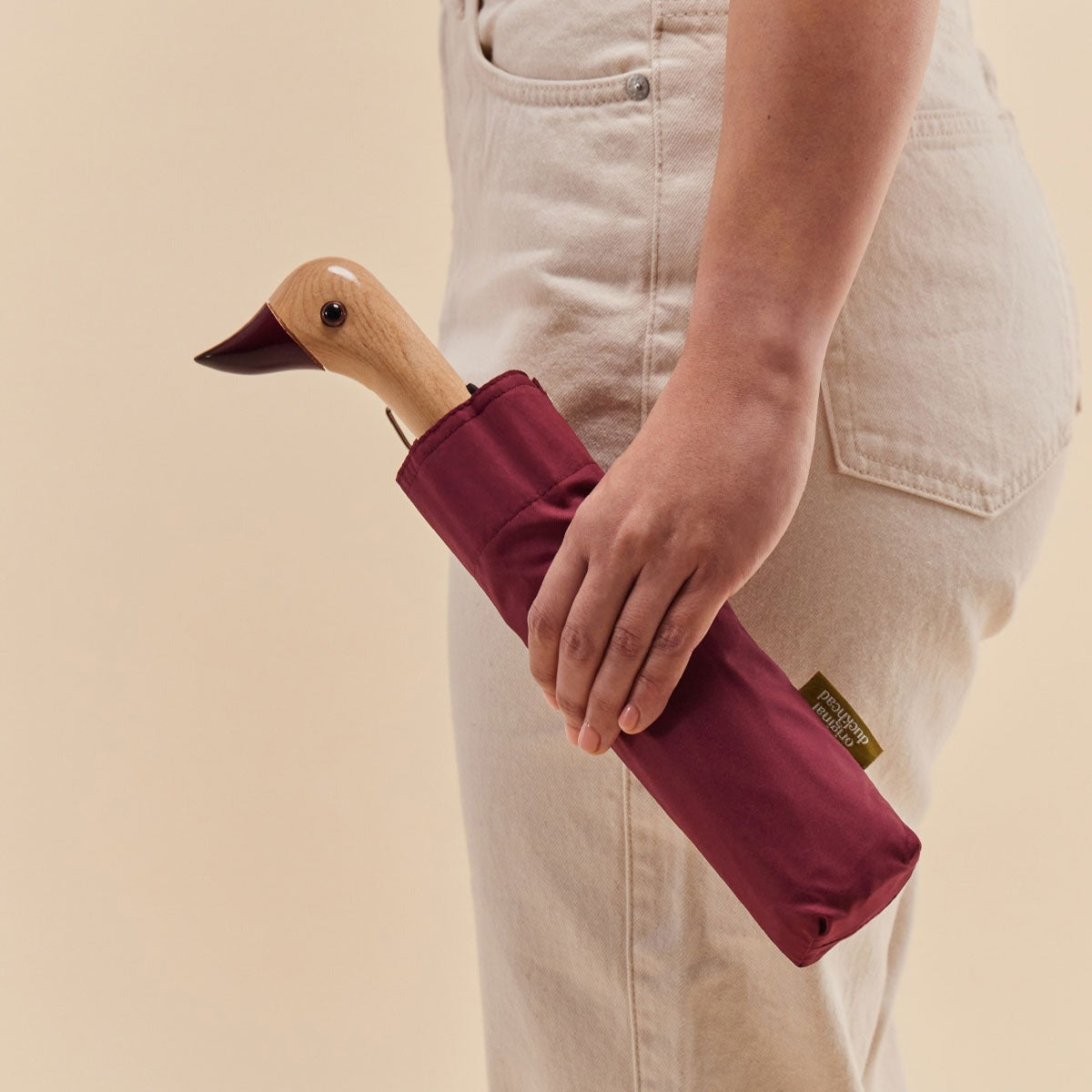 Person holding a cherry duck umbrella with a wooden handle against a beige background