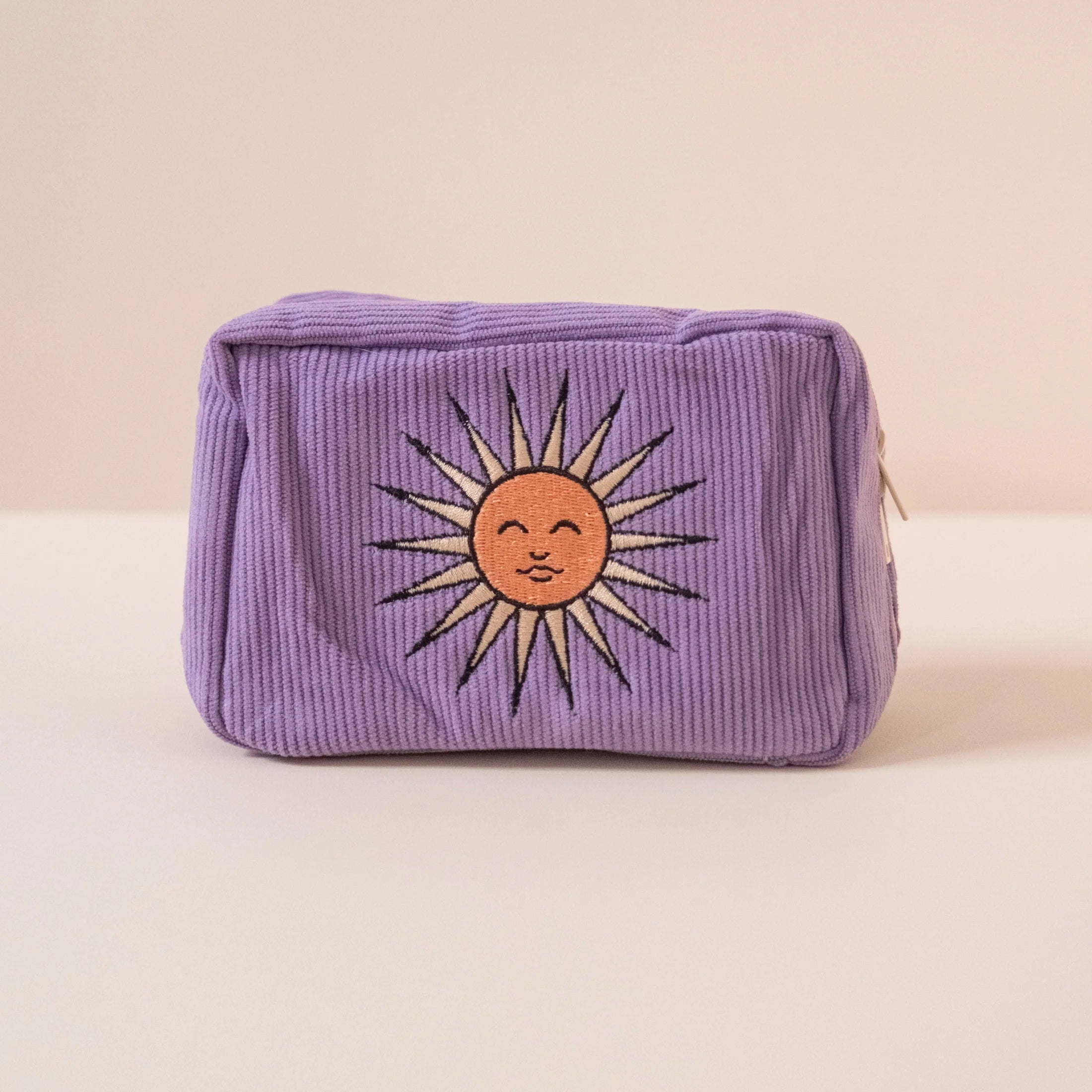 Purple rectangular pouch with a embrodery sun design on a beige background