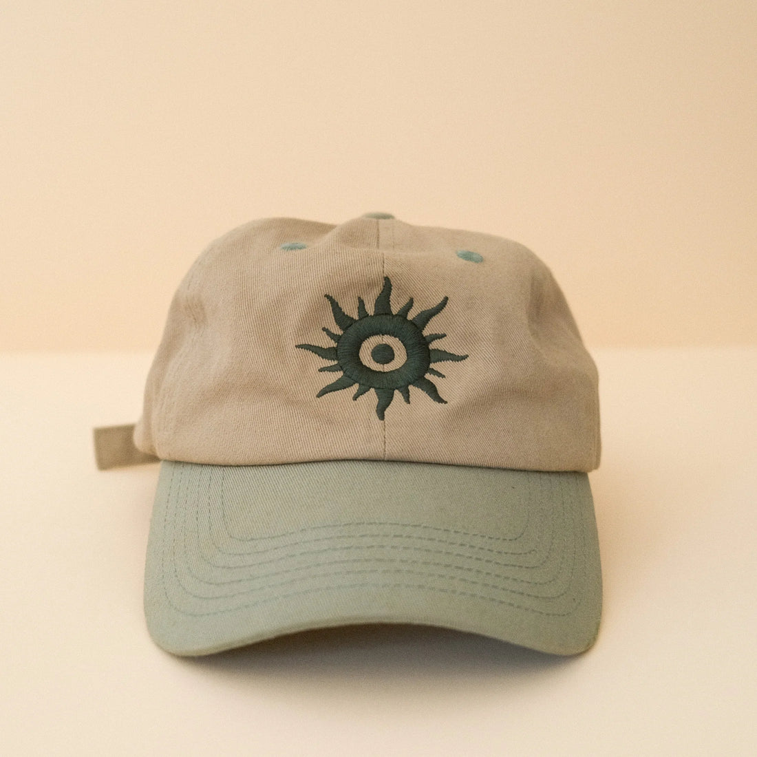 Beige cap with a green sun emblem on the front against a beige background