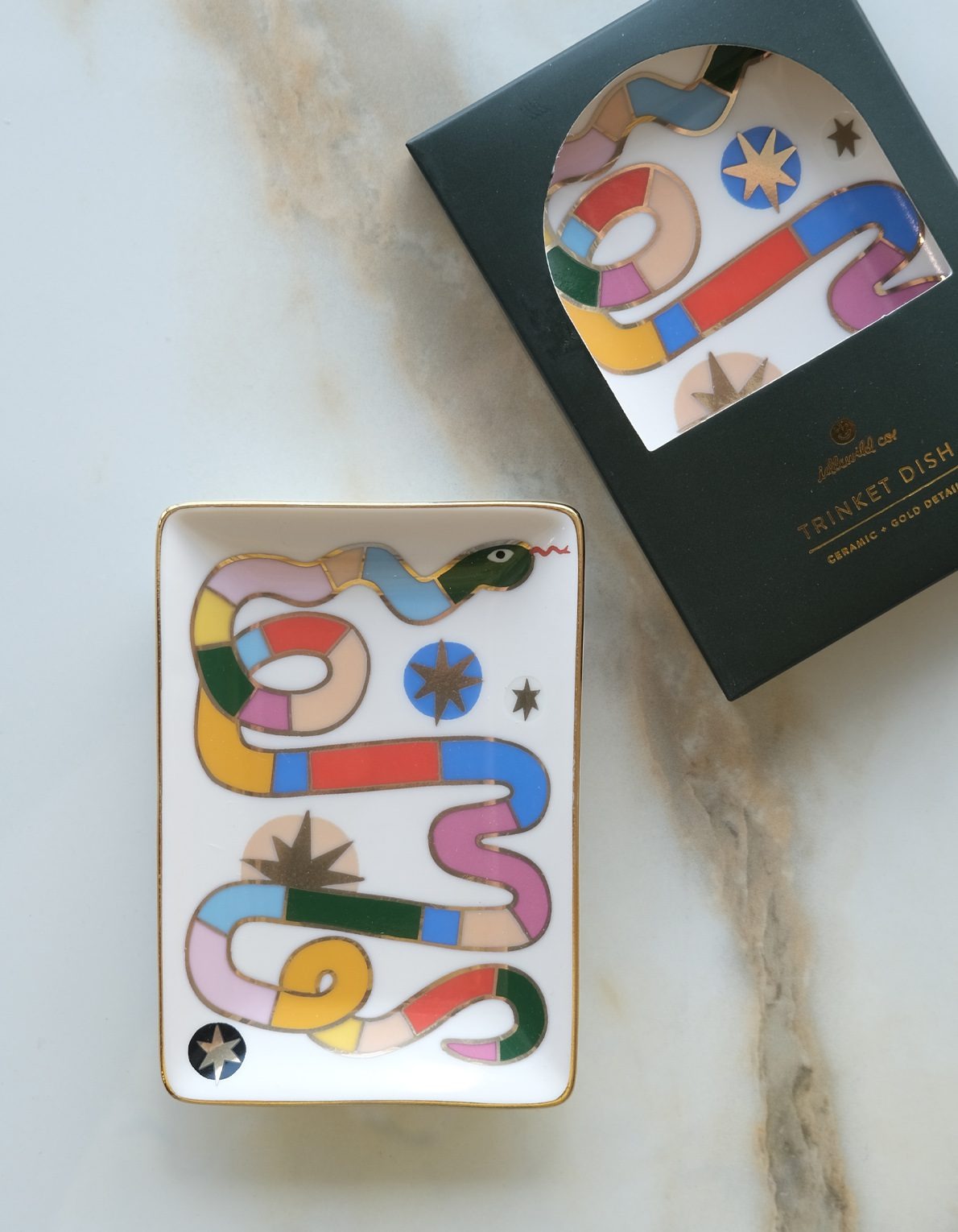Decorative trinket dish with colorful snake design on a marble surface, next to its packaging.