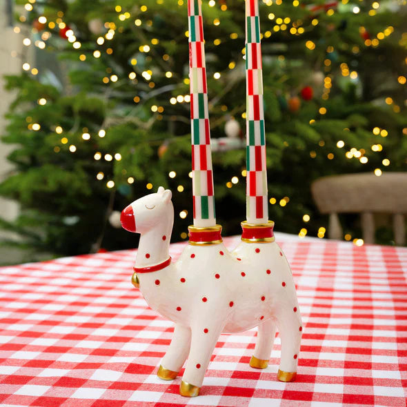 Decorative camel candle holder on a red and white checkered tablecloth in front of a Christmas tree.