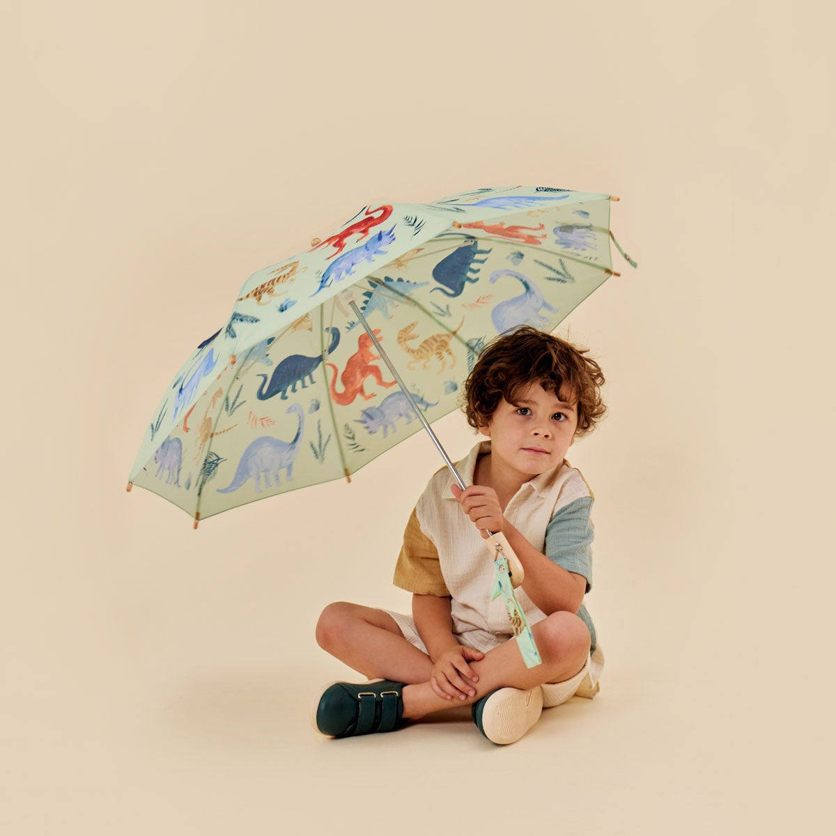 Child holding a colorful umbrella with dinosaur design on a beige background