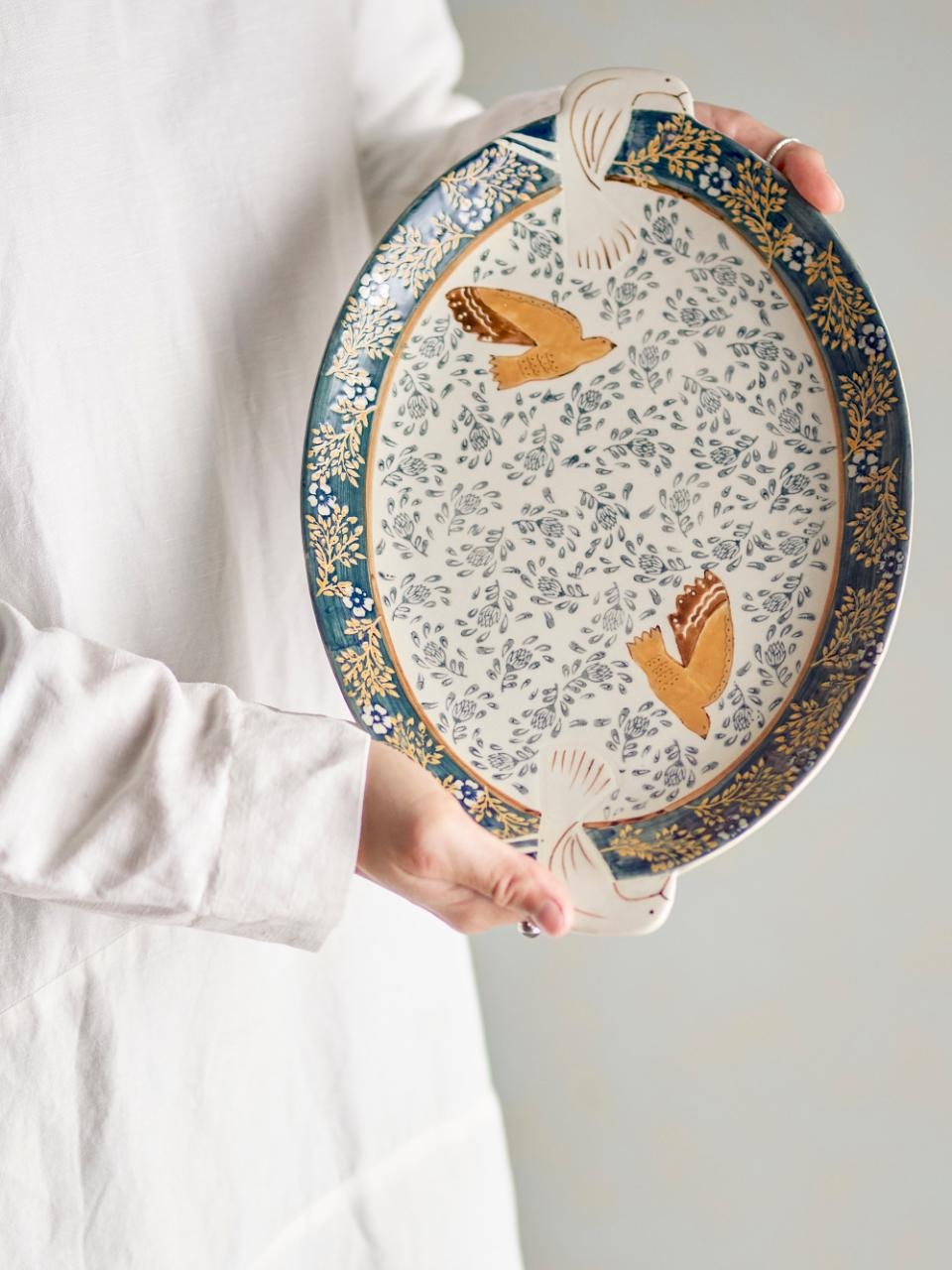 Person holding a decorative ceramic plate with floral and bird patterns.