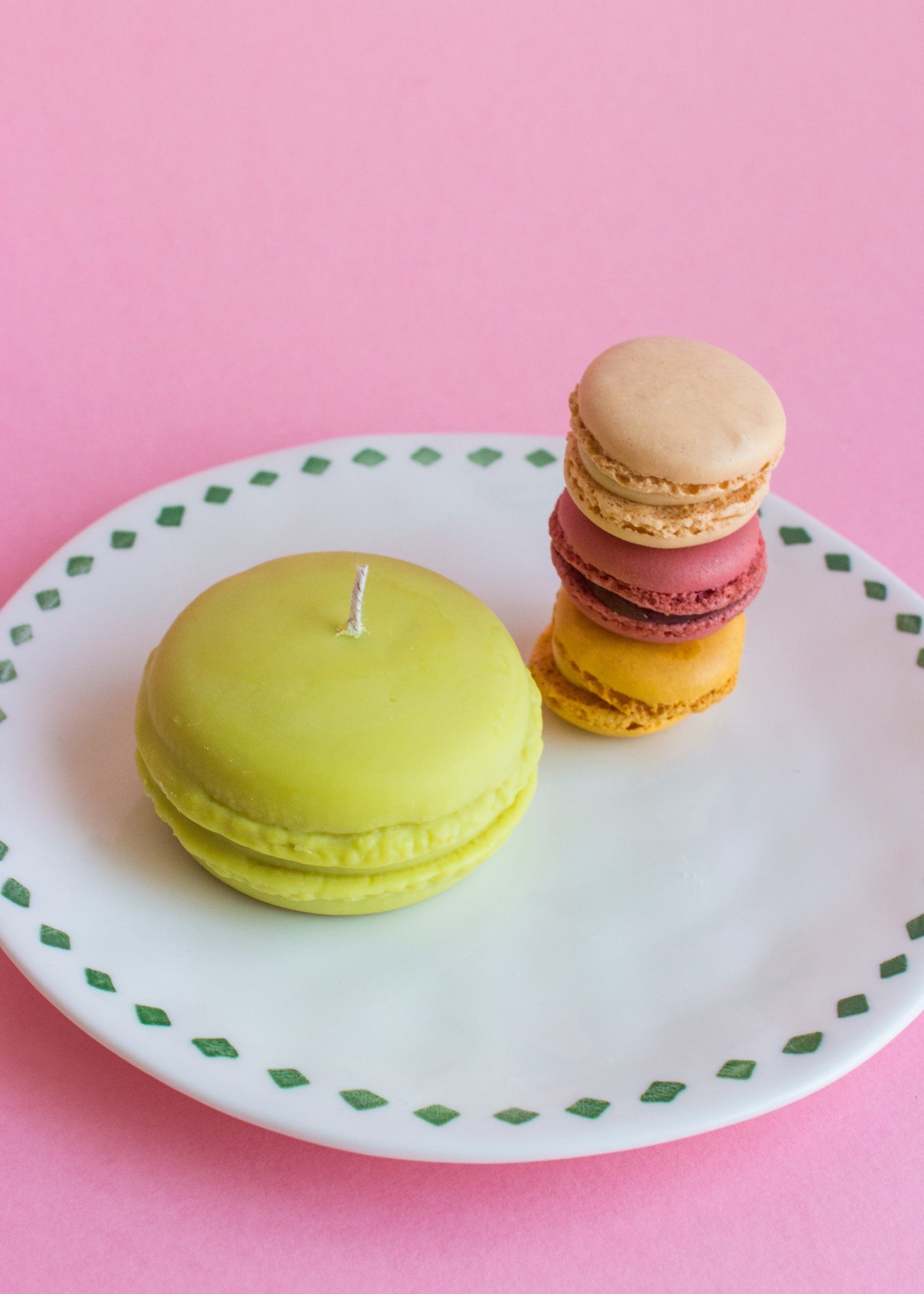 Macaron-shaped candles on a decorative plate with other macarons and a pink background