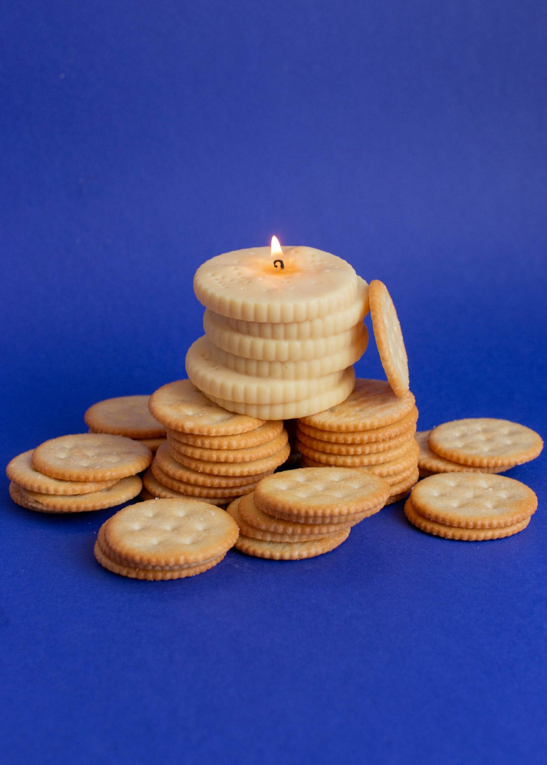 Pile of cheese cracker-shaped soy wax candles with real cheese crackers, styled on a blue background