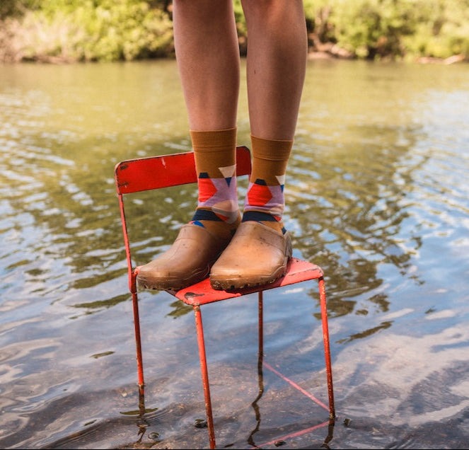 Person standing on a red chair in water wearing brown boots and the kjaleido socks.
