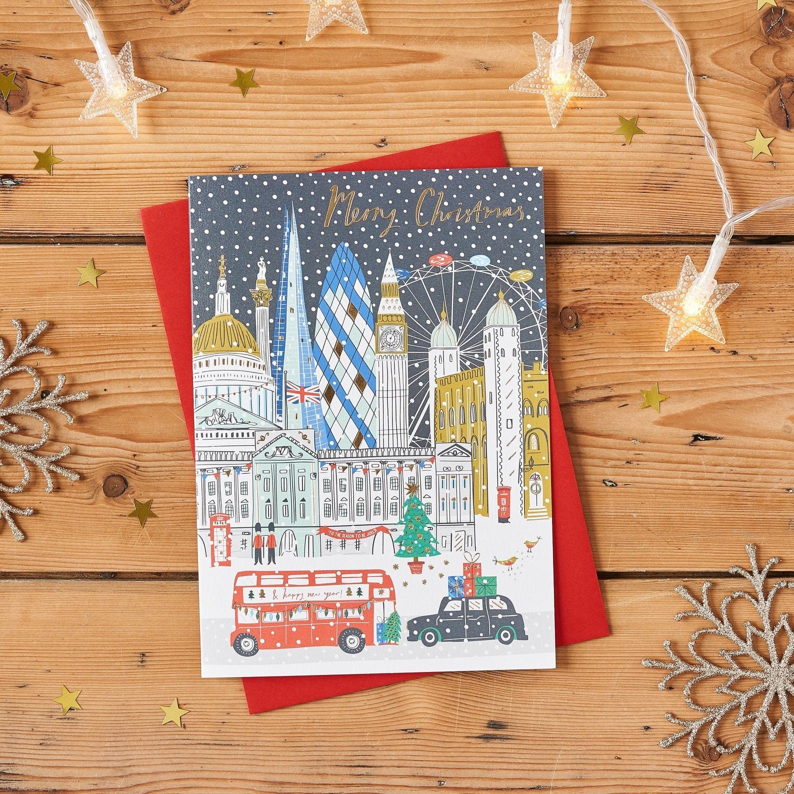 Gold Foiled Christmas Card featuring London landmarks in snow: Big Ben, Tower Bridge, Gherkin, London Eye; on a wooden surface