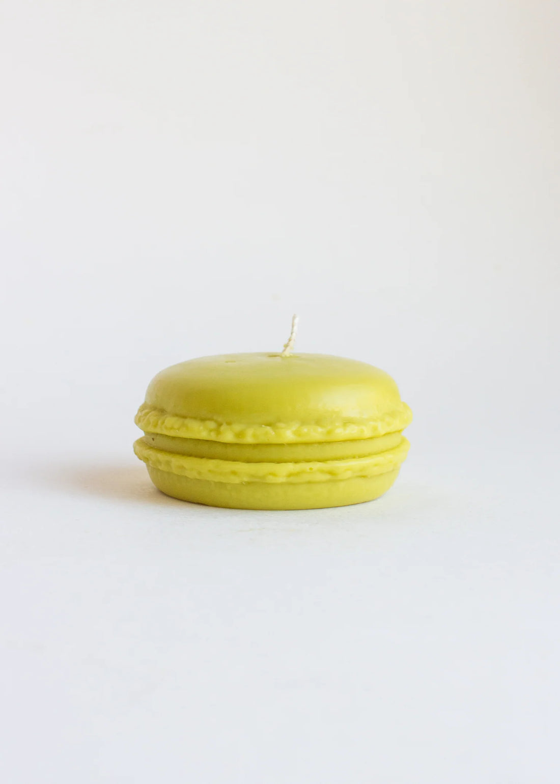 Green candle shaped like a pistache-macaron on a white background