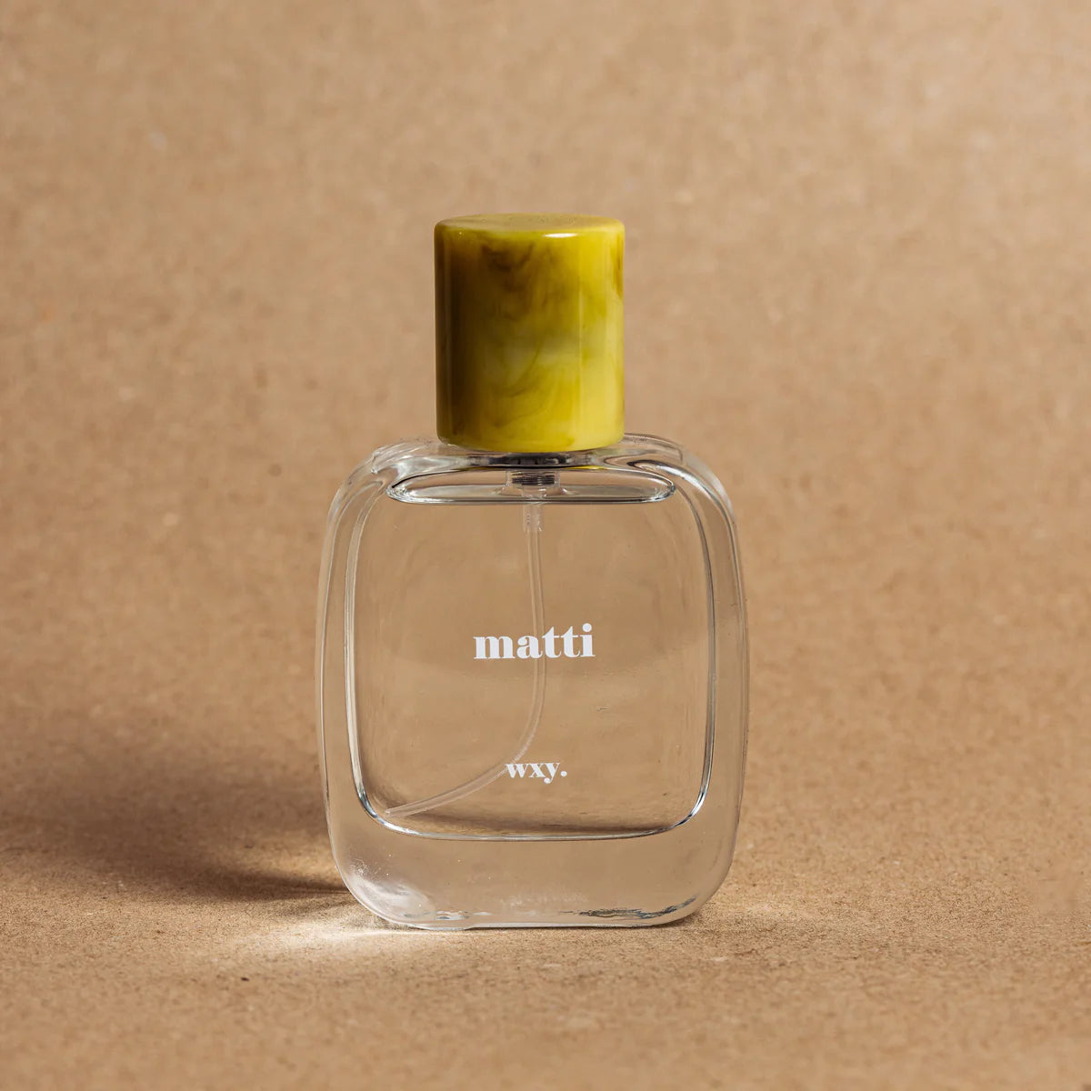 Matti Eau de Parfum bottle on a brown background with a yellow lid – fresh green and woody fragrance