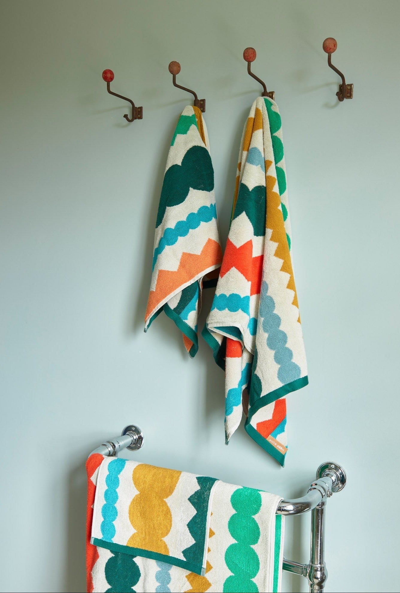Colorful patterned Fizz towels hanging on hooks against a light blue wall.