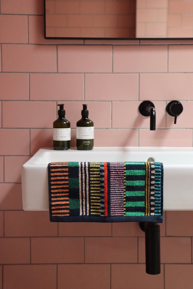 Bathroom sink with a multi stripes colorful towel on a pink tiled wall.