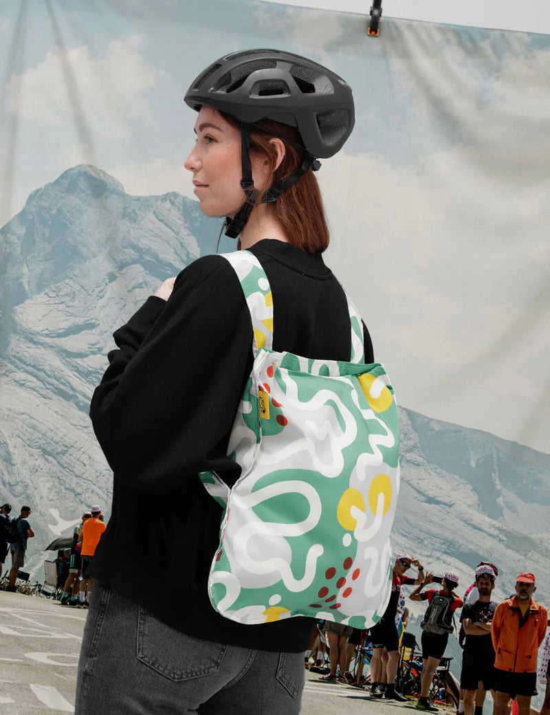 Person wearing a black helmet and carrying a colorful backpack with a mountainous background.
