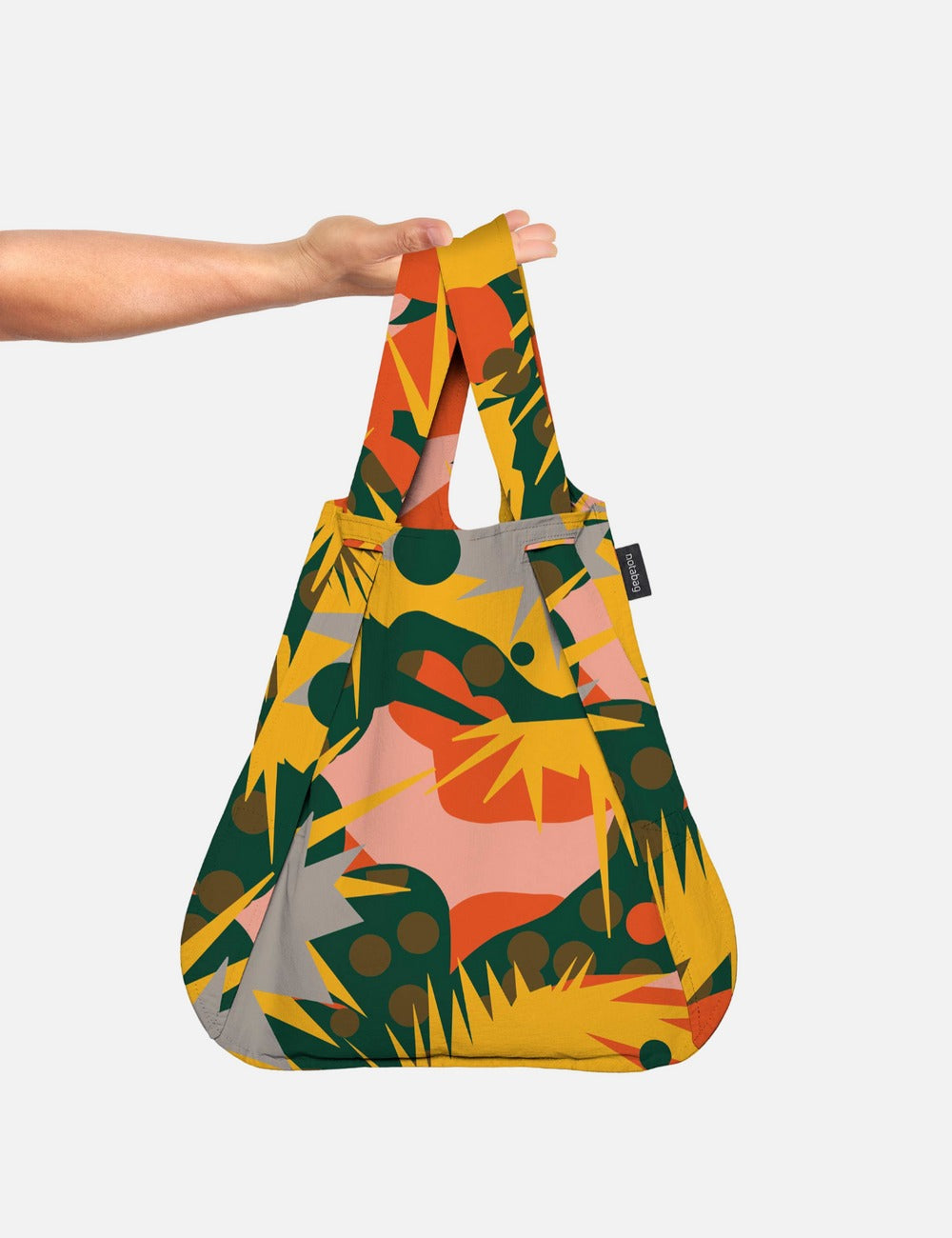 A person holding the multicolored Notabag Spark Bag & Backpack with a floral pattern.