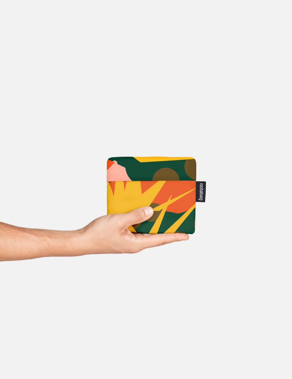 Person holding the multicolored Notabag Spark, shown partially folded into its compact pouch form—functioning as both a stylish tote and hands-free backpack.