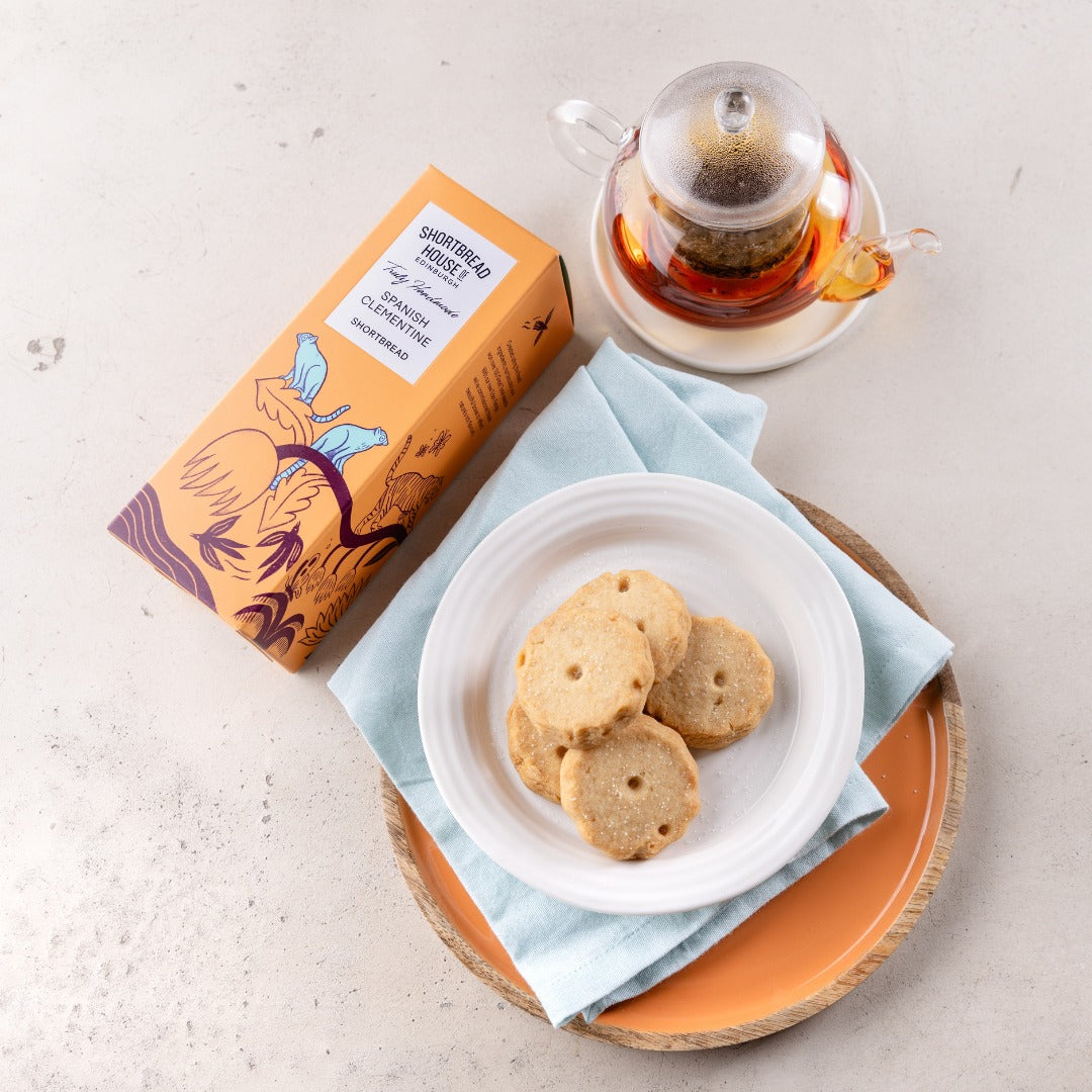 Shortbread cookies on a plate with a box of tea and a cup of tea in the background.