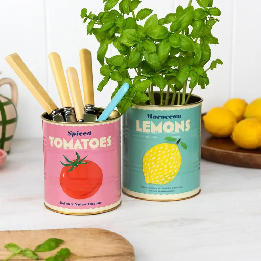 Tomato and lemon storage tins filled with herbs and cutlery on marble countertop