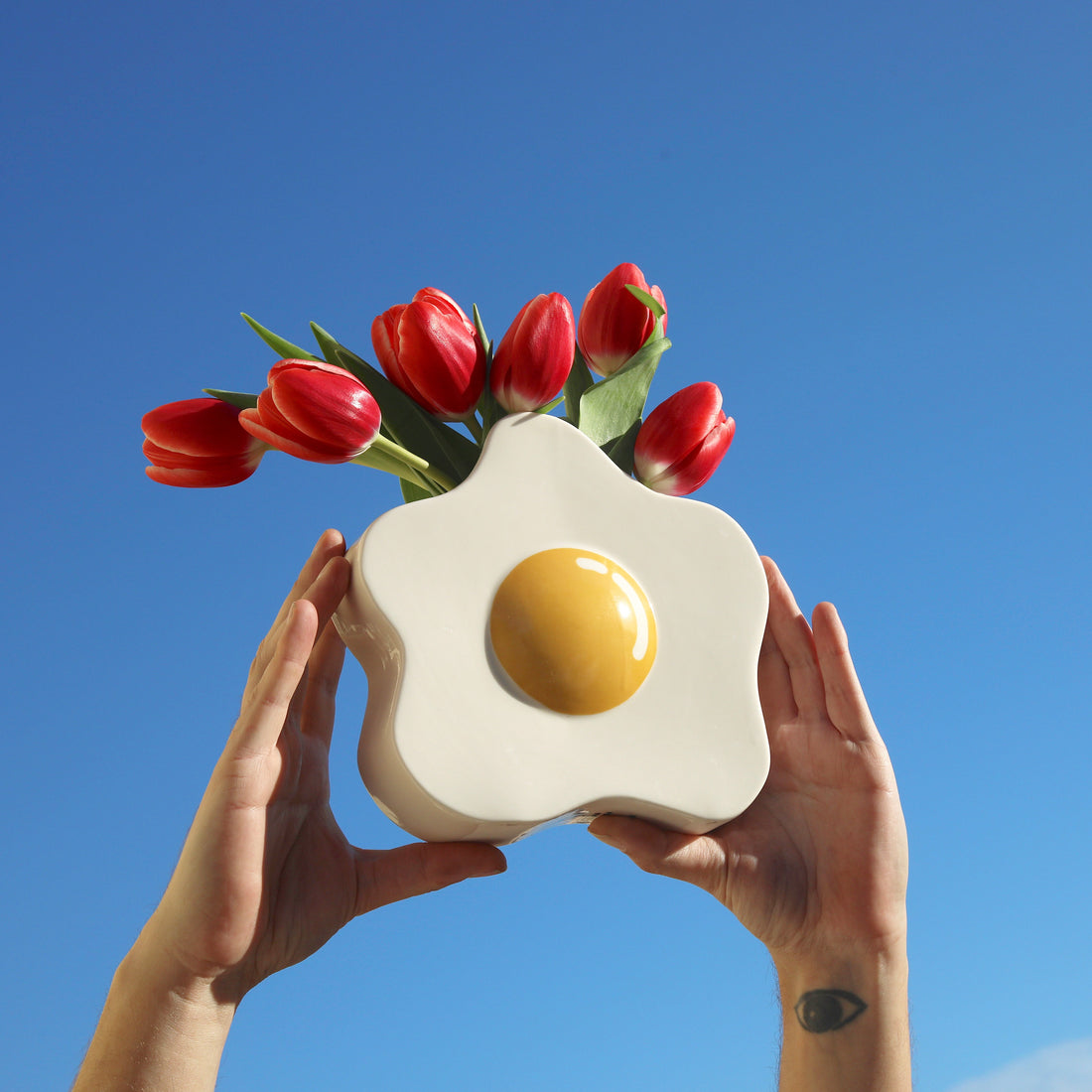 Person holding a white Vase with glossy white base and yellow yolk center against a blue sky