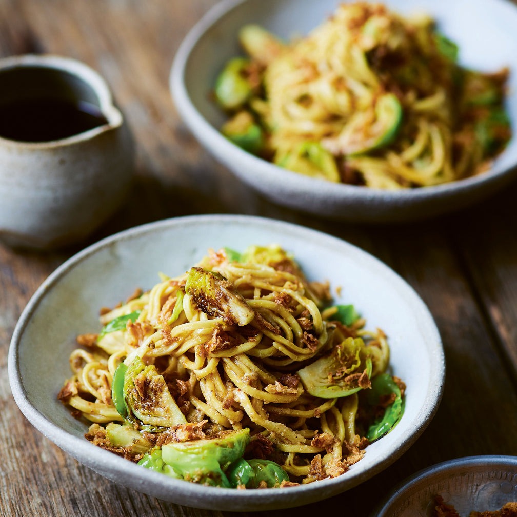 Two bowls of noodles with green vegetables on a wooden table.