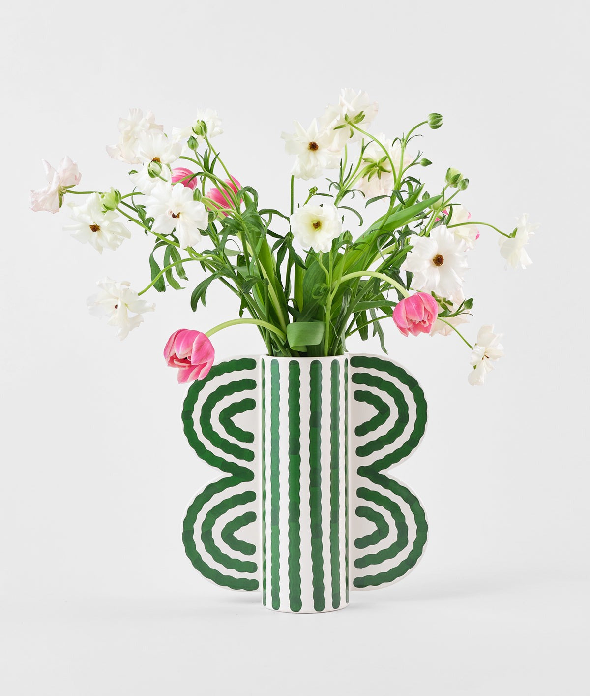 Butterfly Vase by Séverin Millet filled with flowers, off-white ceramic with green wave pattern and wing-shaped handles, set against a white background.
