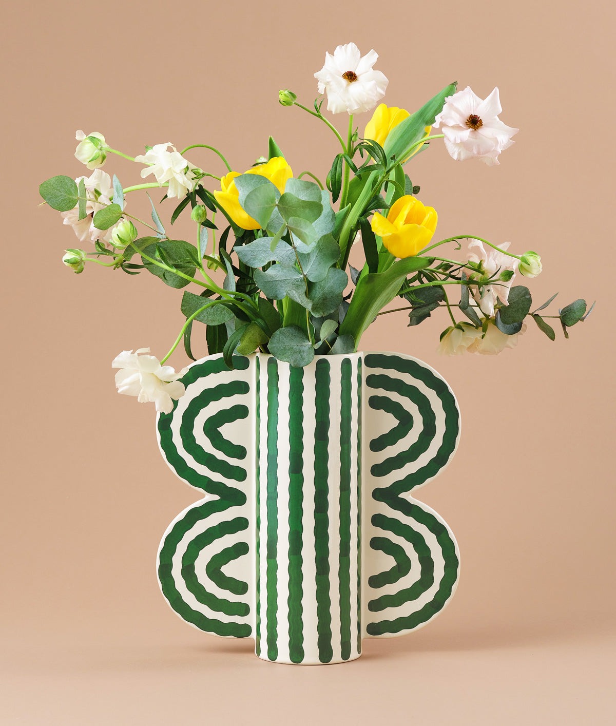 Butterfly Vase by Séverin Millet filled with flowers, off-white ceramic with green wave pattern and wing-shaped handles, set against a brown background.