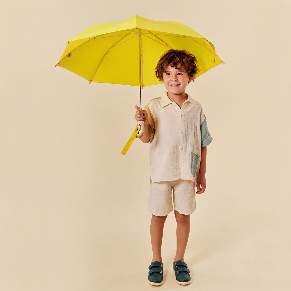 Child holding a yellow umbrella against a beige background