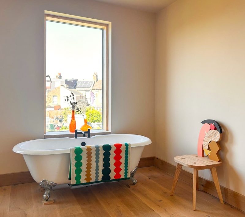 Bathroom with a freestanding bathtub, fizz colorful towel, and a small chair with a decorative backrest.