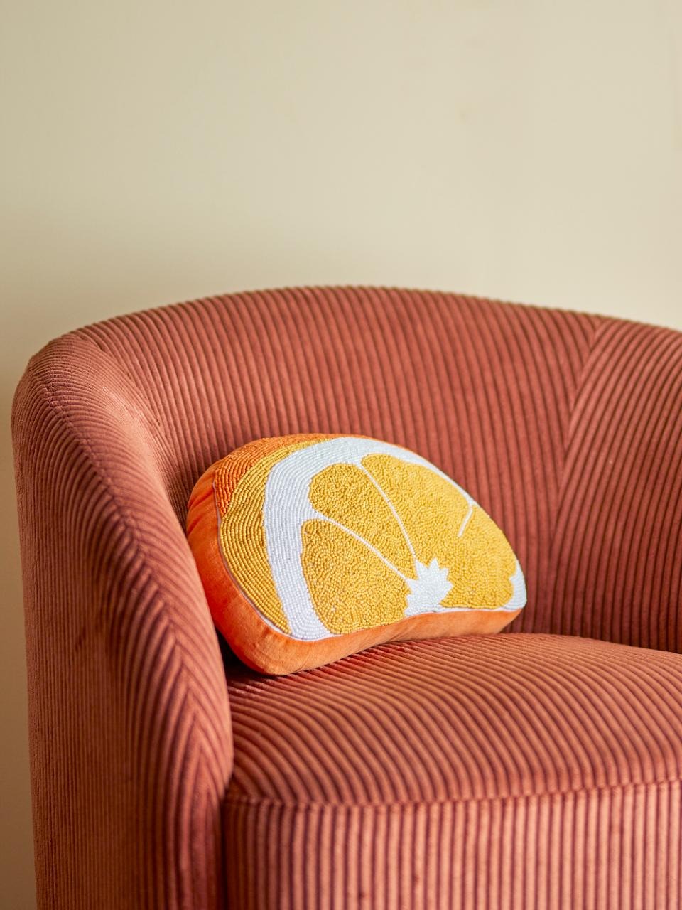 Cushion shaped like a orange on a textured brown chair against a beige wall