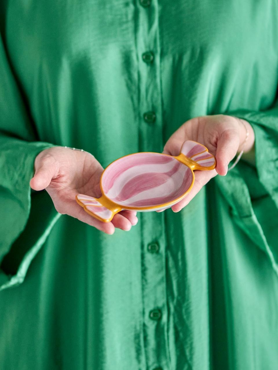 Person holding n Caramella-shaped serving plate rose small against a green shirt background