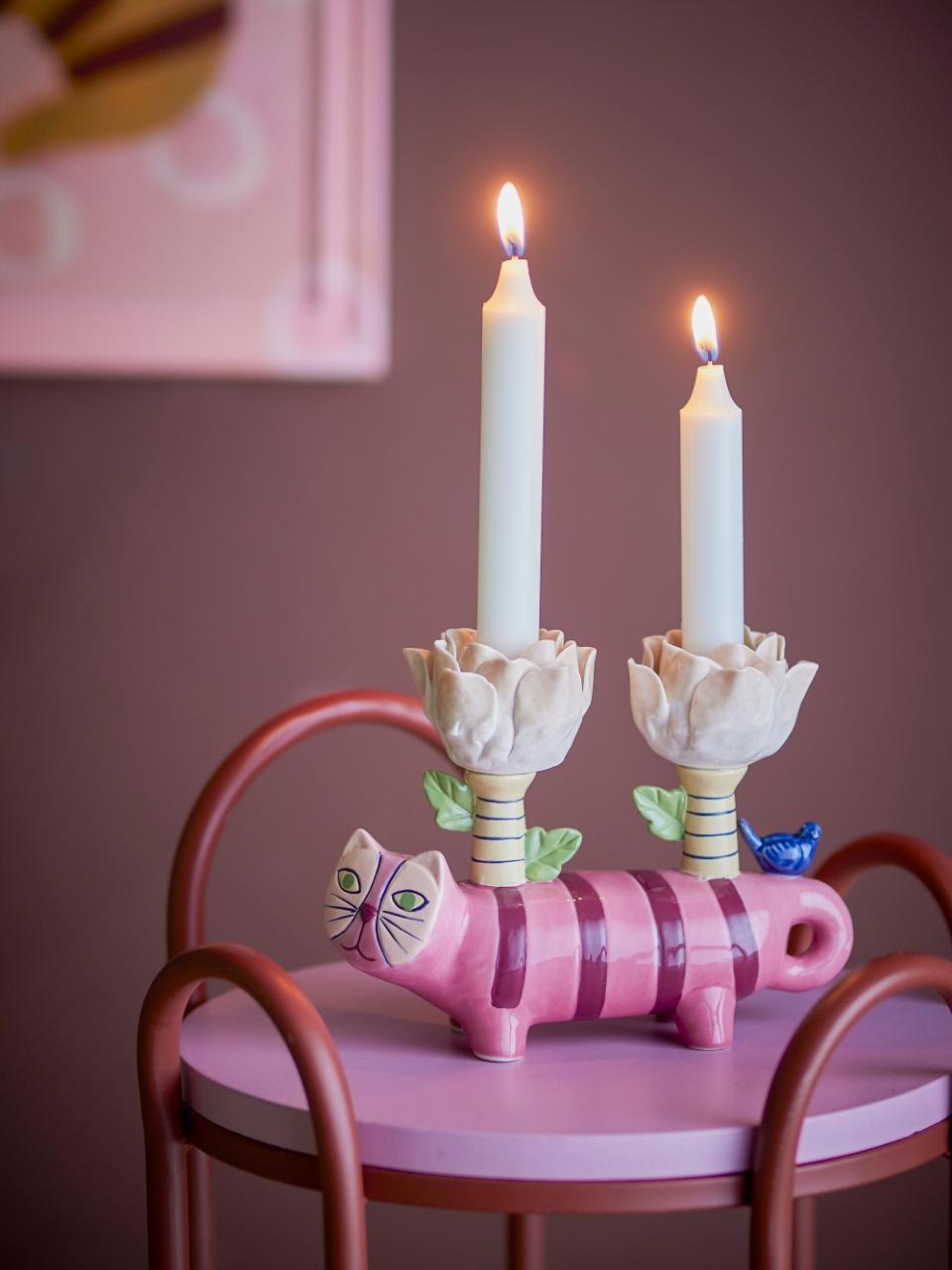 PInk cat-shaped candle holder with two lit candles on a table against a pink wall.
