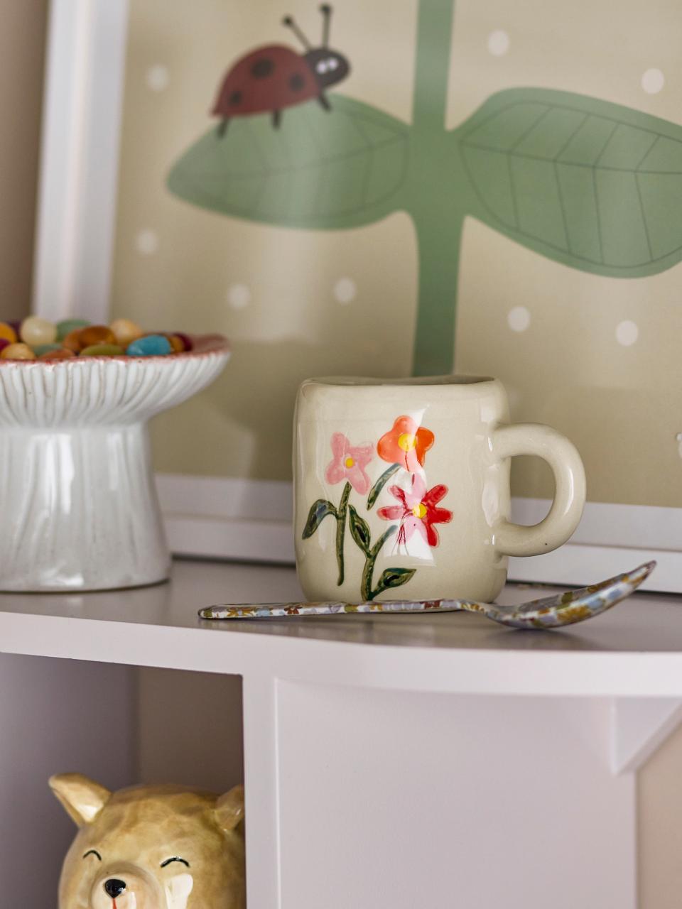 Ceramic mug with floral design on a shelf with a ladybug and leaf decoration in the background.