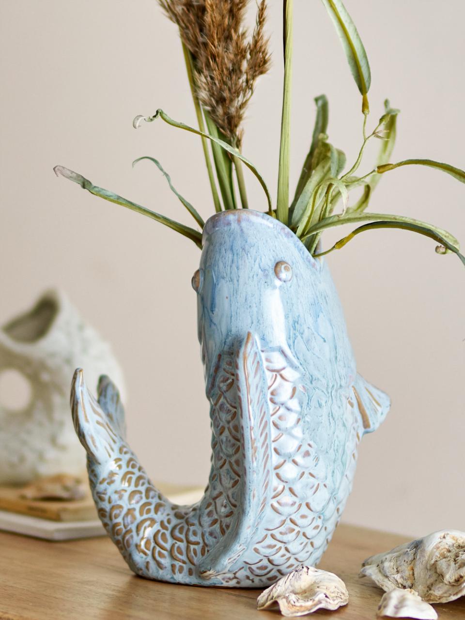 Hiro Fish-Shaped Vase in light blue stoneware, with textured scales and flowing form, displaying flowers on a wooden surface. Coastal-inspired decorative vase suitable as a centerpiece or sculptural accent.