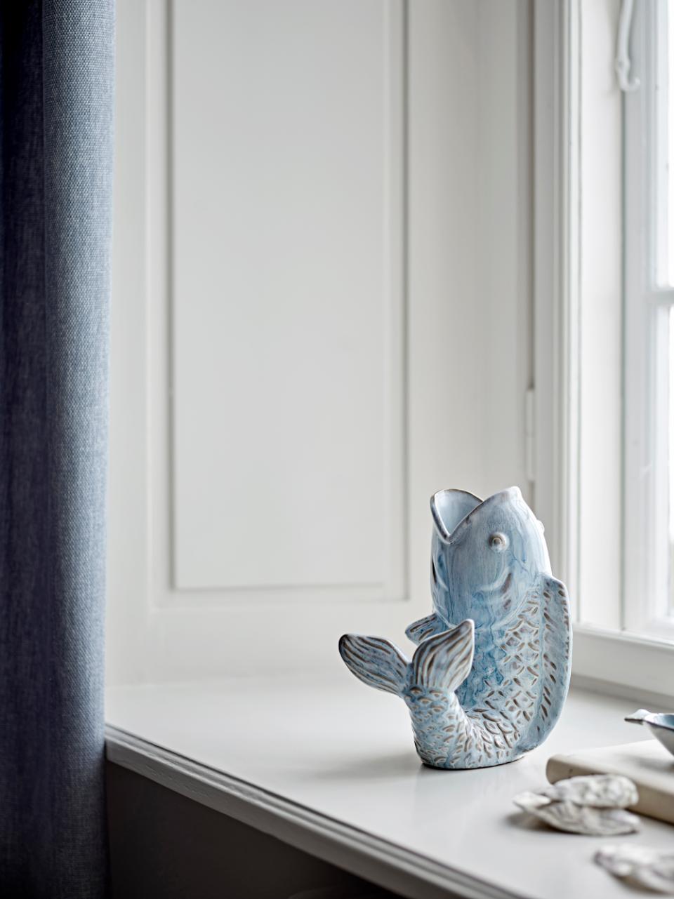 Hiro Fish-Shaped Vase in light blue stoneware, with textured scales and flowing form, on a white windowsill. Coastal-inspired decorative vase suitable as a centerpiece or sculptural accent.