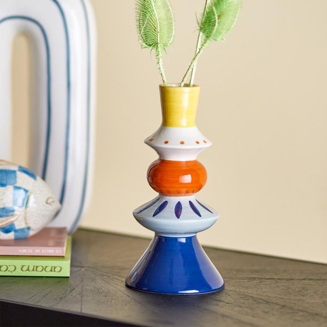Kairi Blue Stoneware Vase – tall ceramic vase with stacked shape and hand-painted yellow, orange, and blue pattern, displaying flowers on a table with a grey background