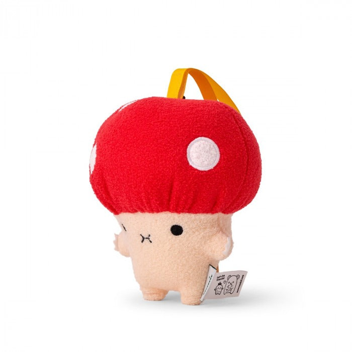 A plush toy resembling a mushroom with a beige body and a bright red cap with white spots. It has an embroidered face and a small yellow tag on its cap.