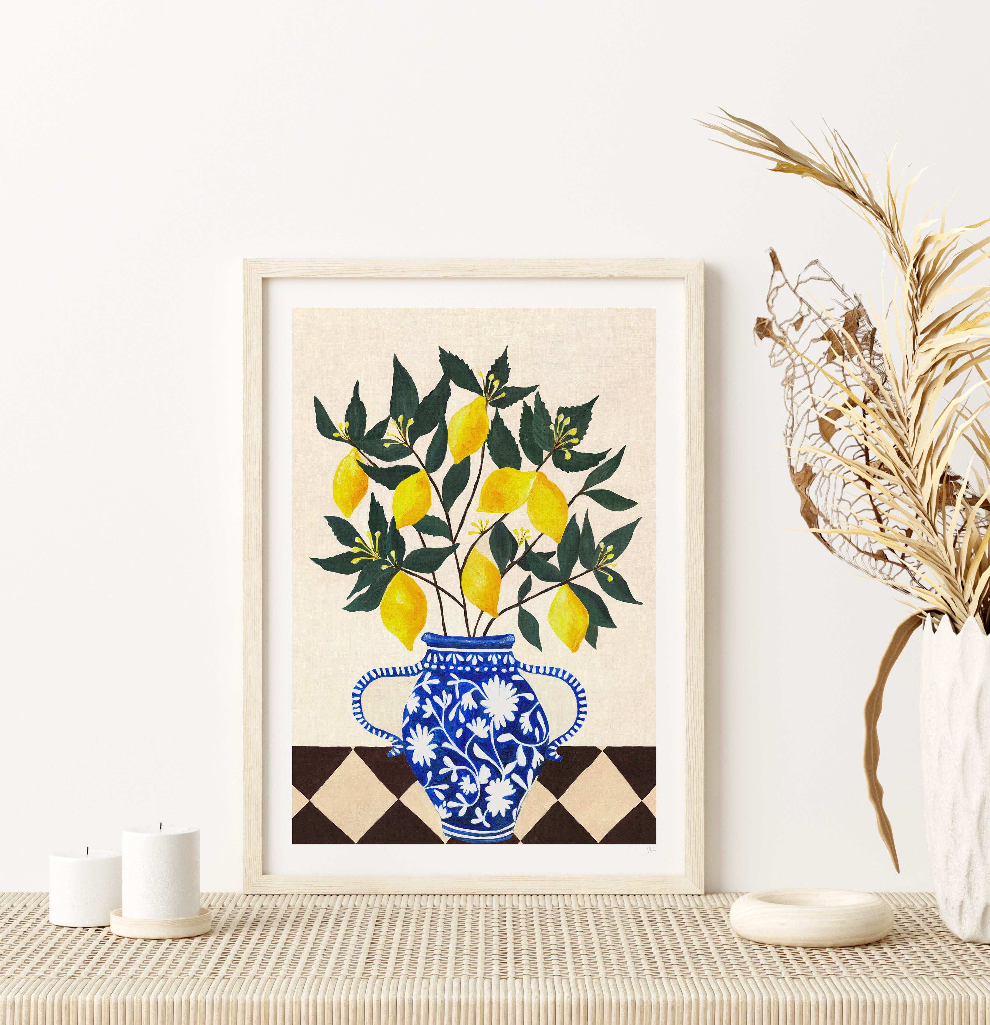 Framed artwork of lemons in a blue floral vase on a table with decorative elements.