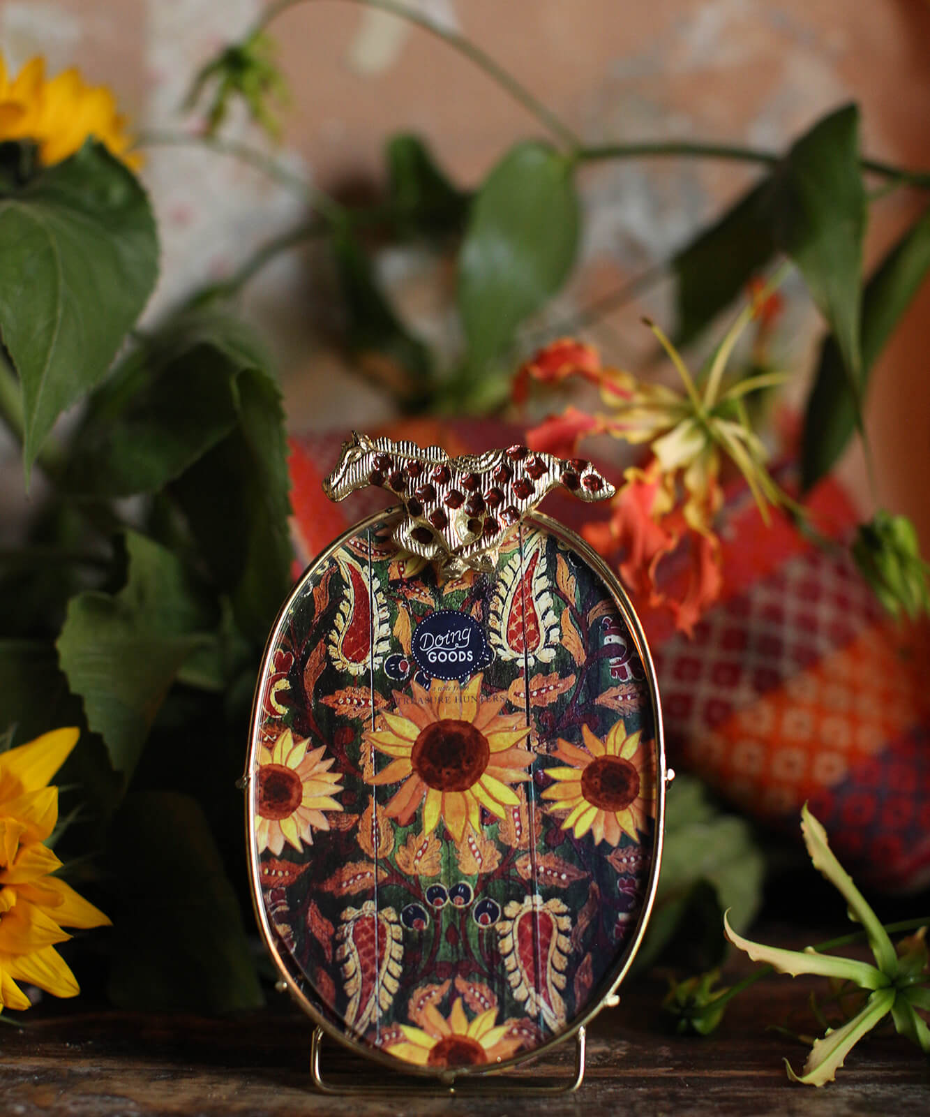 Handcrafted oval brass picture frame with wild horse motif, styled on shelf with greenery for sustainable décor.